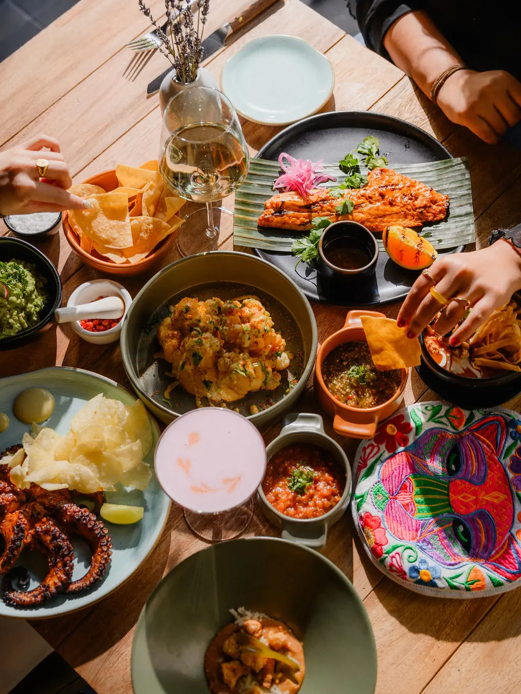 A spread of dishes, tortilla chips, sauces and drinks on a table at Acuyo.