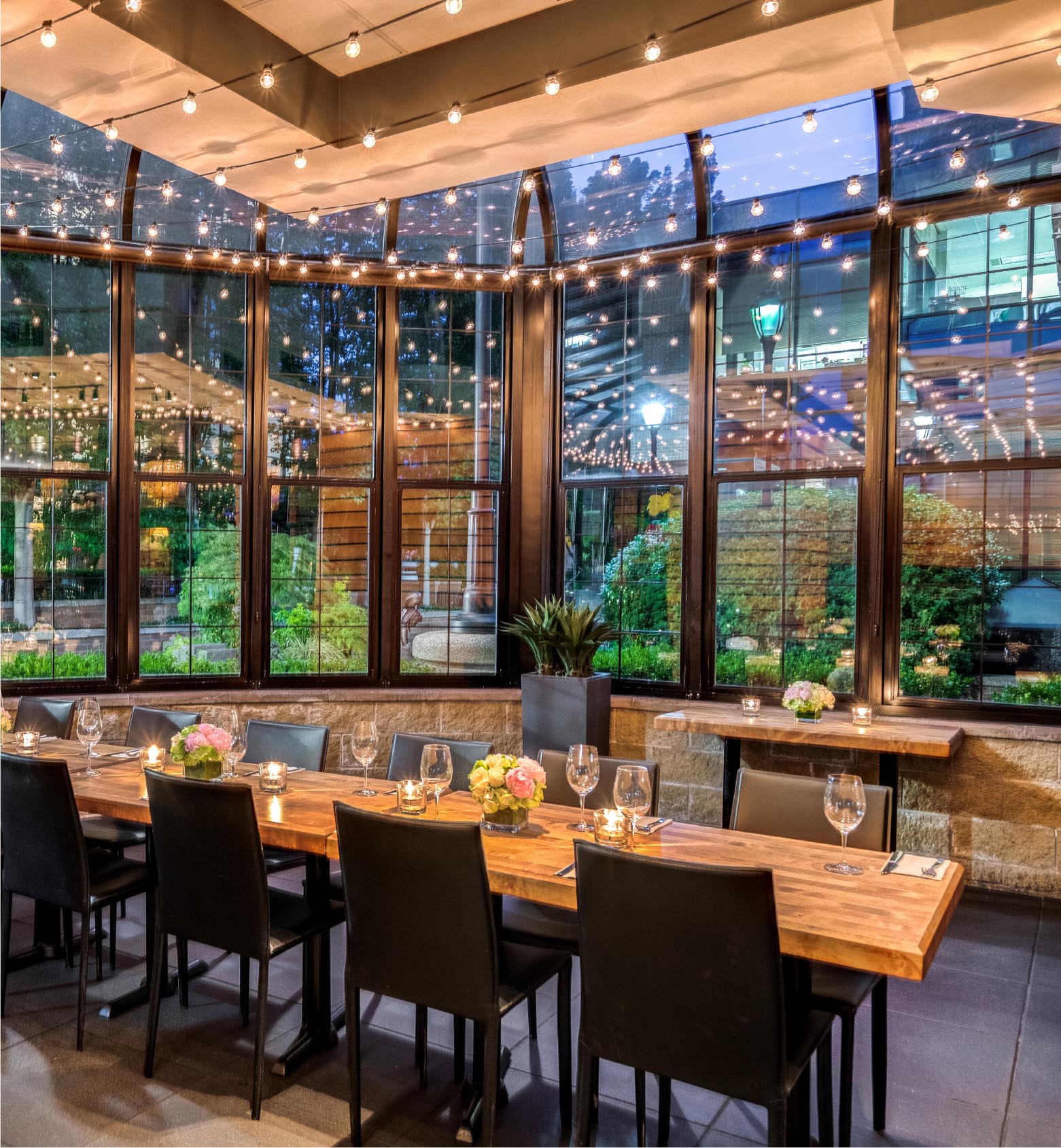 A long dining table beneath string lights and large windows at Cactus Club Cafe Broadway and Granville.