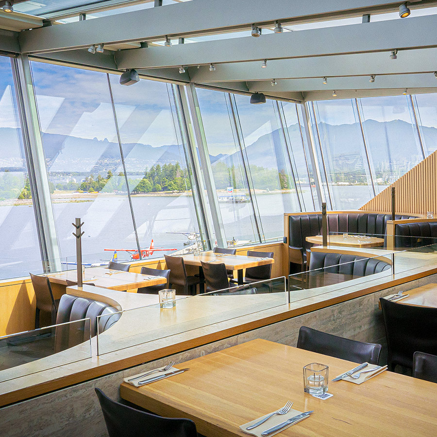 Tables and booths beside tall windows overlooking the harbour at Cactus Club Cafe Coal Harbour.