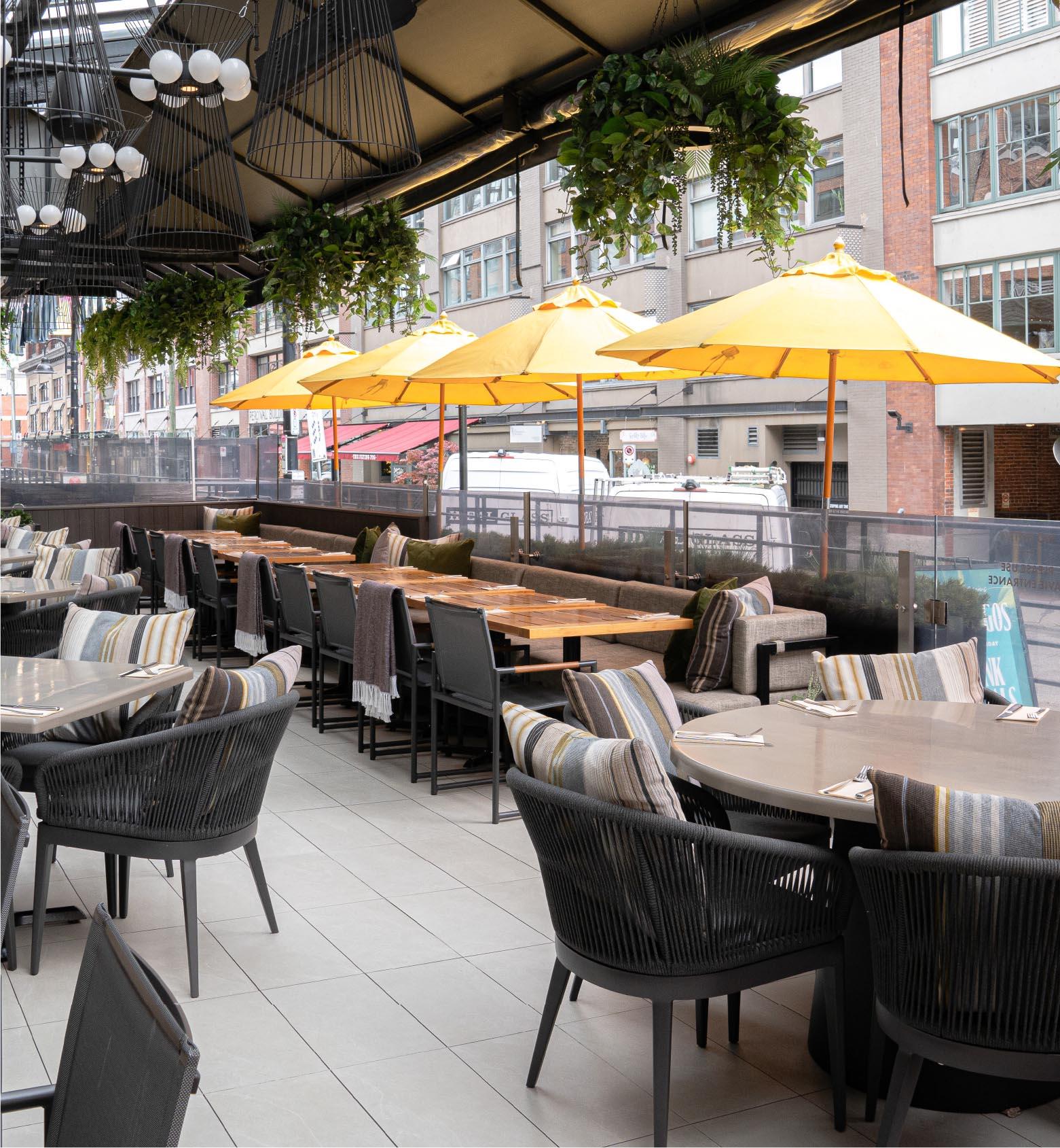 Tables, woven chairs, hanging plants and yellow umbrellas on the patio at Cactus Club Cafe Yaletown.