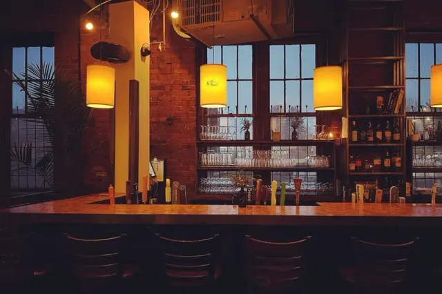 Bar seating and hanging lights beside the tall windows at Alibi Room.