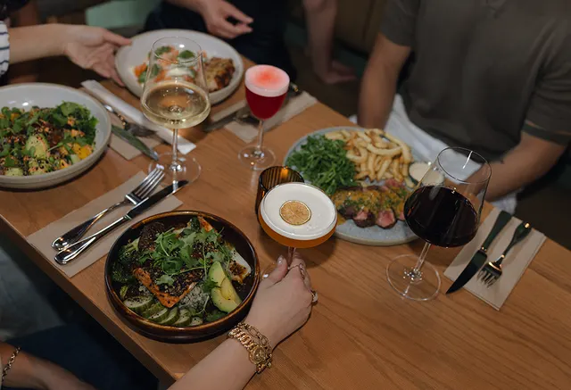 Plates of food and cocktails shared around a table at BREWHALL.