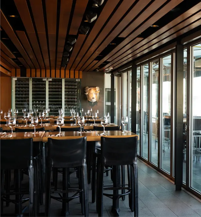 Dining tables, dark chairs and large windows inside Cactus Club Cafe English Bay.