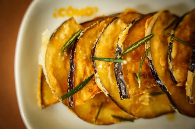 A plated dish with golden slices and herbs at Como Taperia.