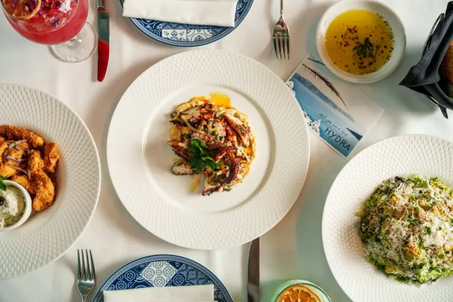 Seafood dishes and drinks on a table with Hydra-branded materials at Hydra Estiatorio.