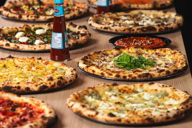 Several pizzas arranged on a table in an official Ignite Pizzeria photograph.