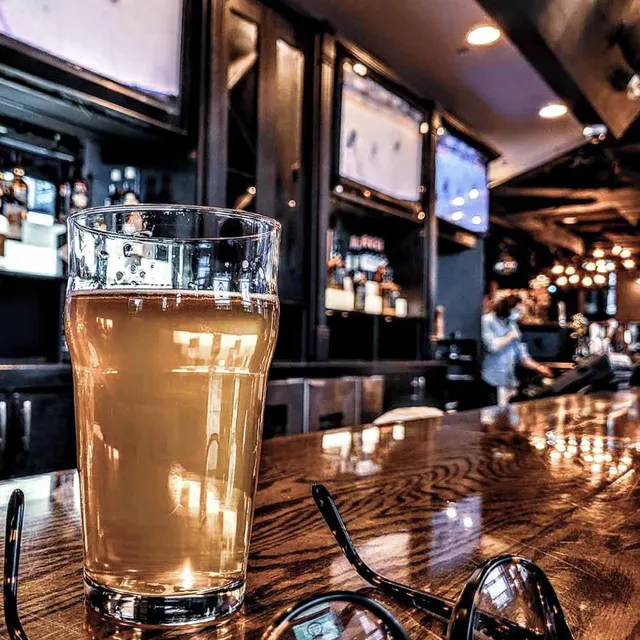 A glass of beer on the wooden bar with televisions and bottle shelves behind it at Library Square Public House.