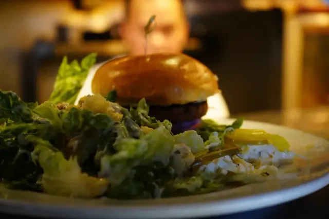 Burger served beside leafy greens on a plate.