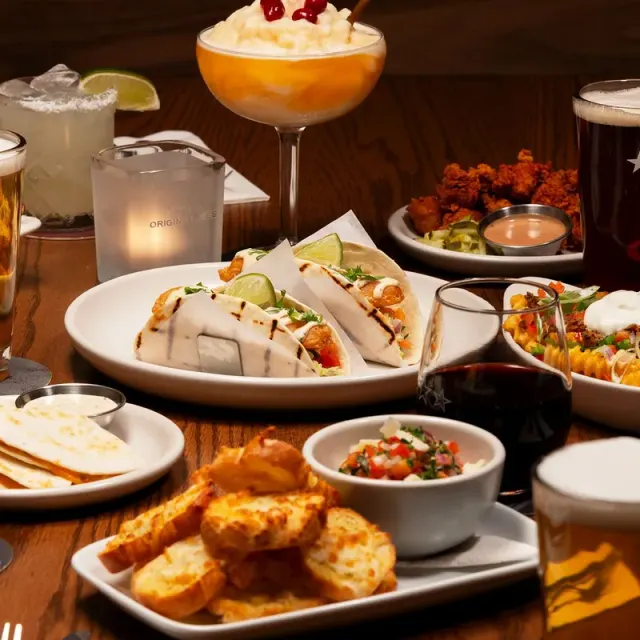 A table of Original Joe's dishes and drinks: fish tacos, fried chicken, quesadillas, garlic bread, beer, a margarita and red wine, beside a candle holder printed Original Joe's.