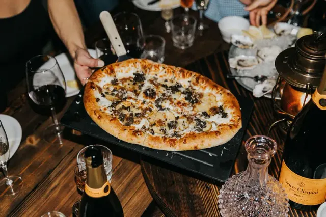 Pizza being served over a table set with drinks and dishes.