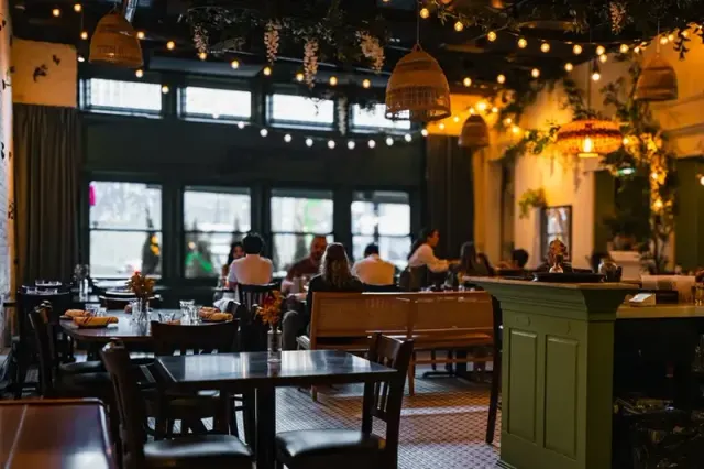 Restaurant dining room with wooden tables, warm lighting and a bar.