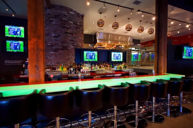 Sports-bar interior with stools, a long counter and television screens.