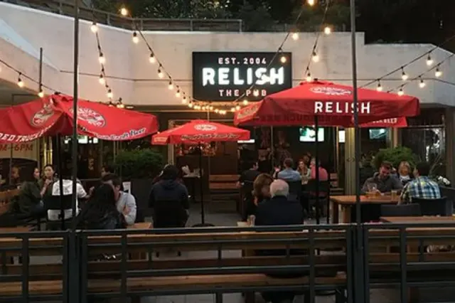 Pub patio with red umbrellas beneath a Relish sign.