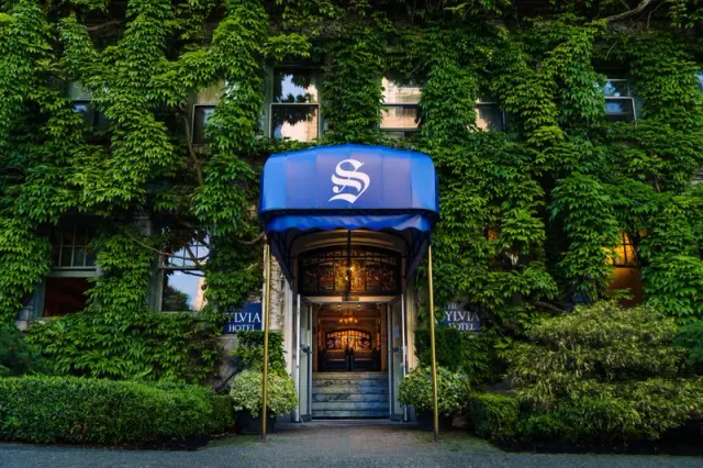 Hotel entrance with a blue canopy surrounded by an ivy-covered facade.