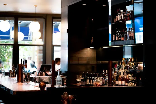 Restaurant bar with illuminated bottle shelves and pendant lights.