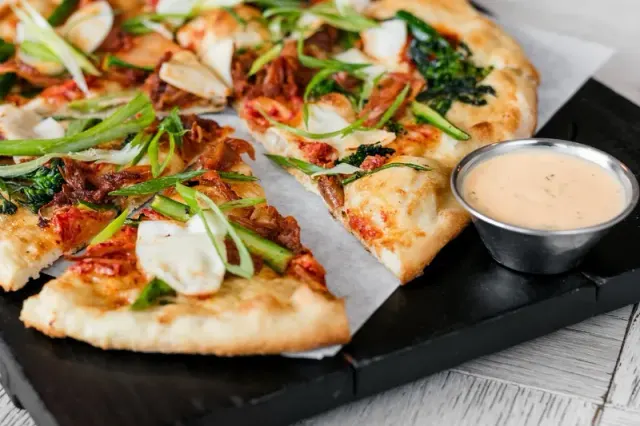 Sliced pizza with tomatoes and greens, served beside a dipping sauce.