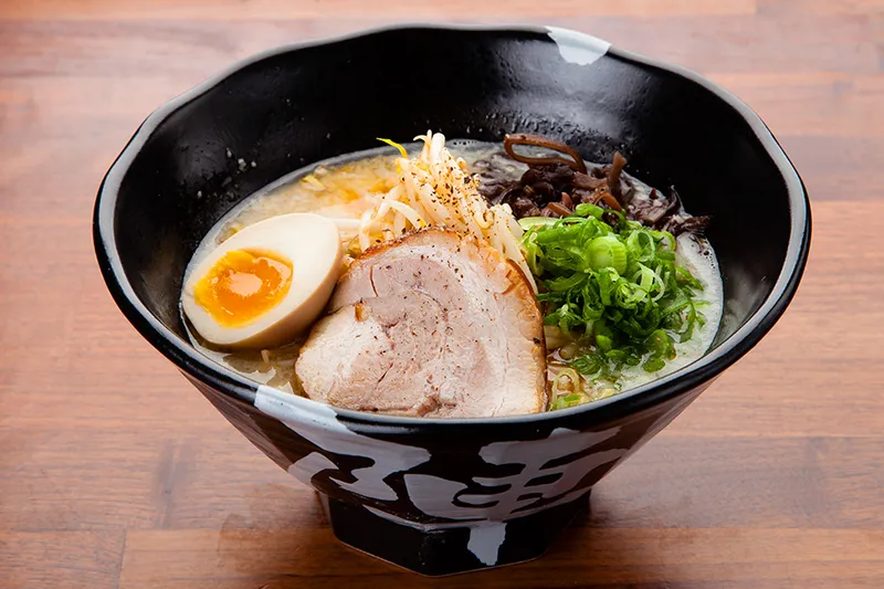 A bowl of ramen with egg, meat and vegetables in an official JINYA photograph.