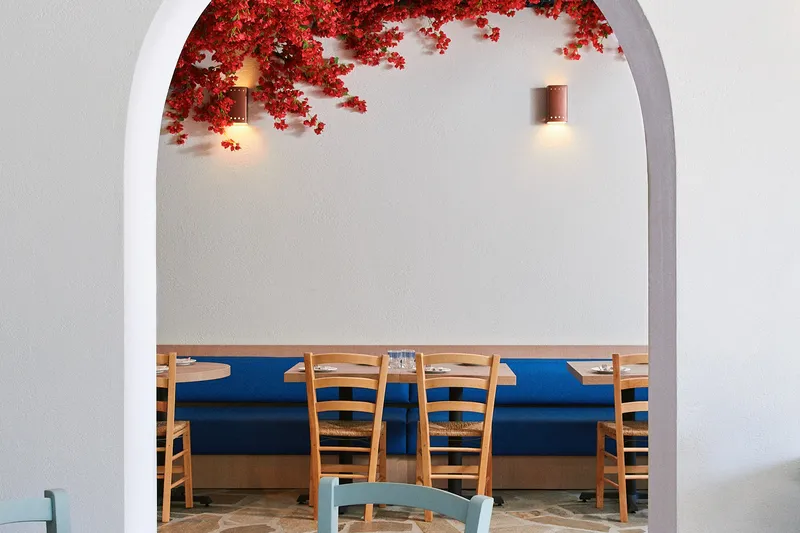 Tables and blue banquette seating framed by an archway at Loula’s Taverna.