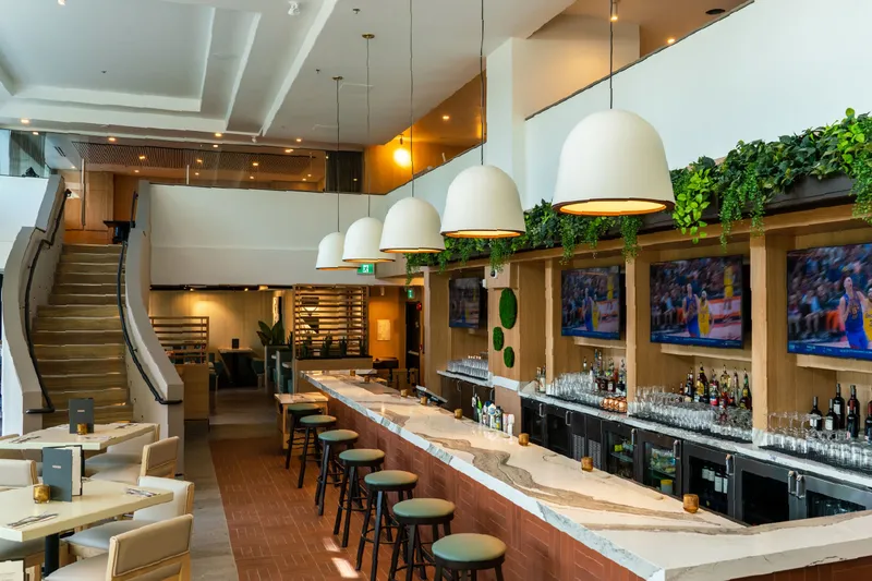 Bright restaurant interior with a long bar, stools and pendant lights.