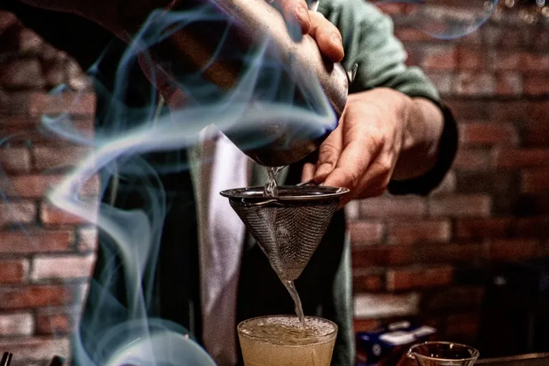 A drink being poured through a strainer into a glass.