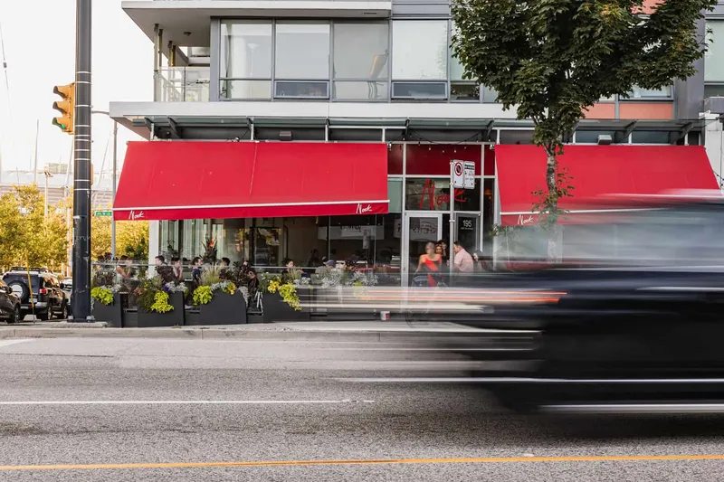 Restaurant frontage with red awnings viewed from across the street.