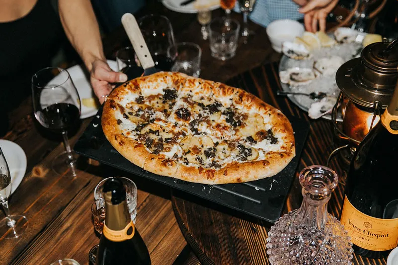Pizza being served over a table set with drinks and dishes.