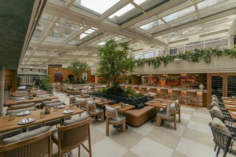 Dining and lounge seating beneath a glass roof with greenery.