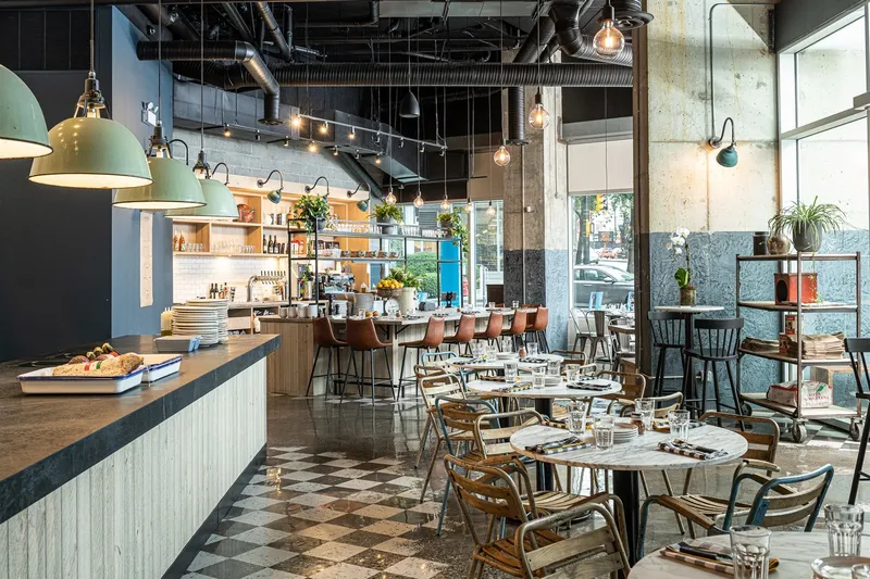 Restaurant dining room with wooden tables, bar seating and hanging lights.