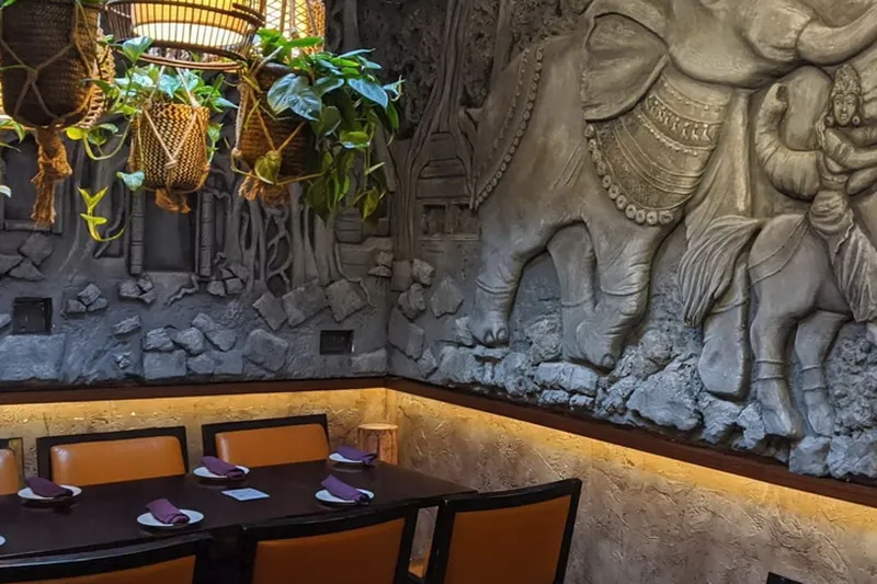 Restaurant booth seating beside plants and a carved wall relief.