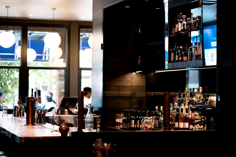 Restaurant bar with illuminated bottle shelves and pendant lights.