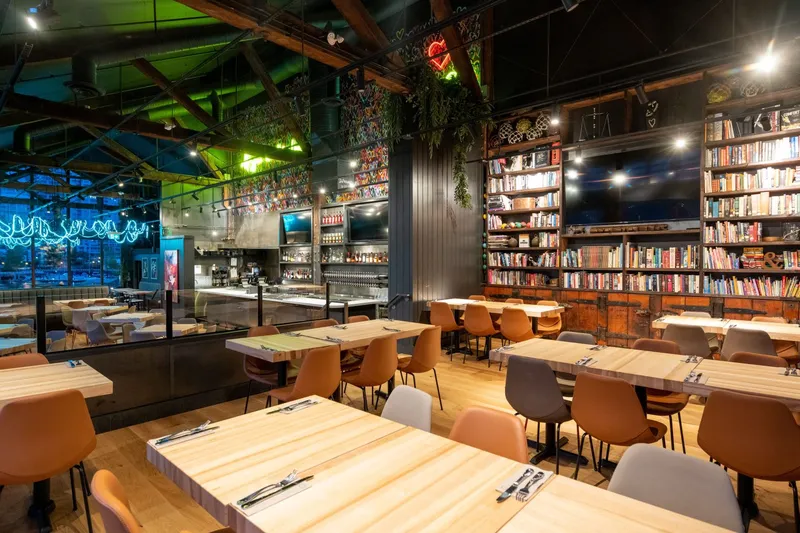 Restaurant dining room with tables, bar shelving and warm lighting.