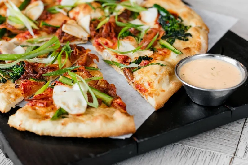 Sliced pizza with tomatoes and greens, served beside a dipping sauce.