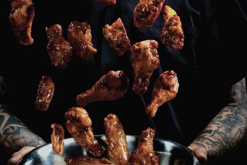 Sauced chicken wings being tossed above a pan.