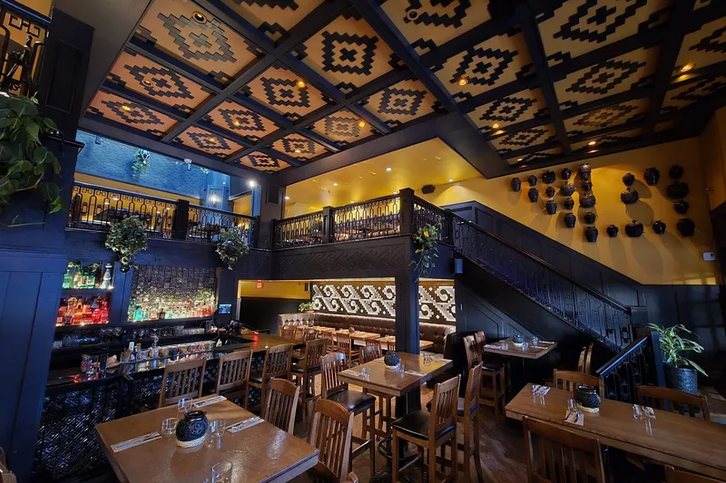 Restaurant interior with patterned ceiling panels, tables and bar seating.